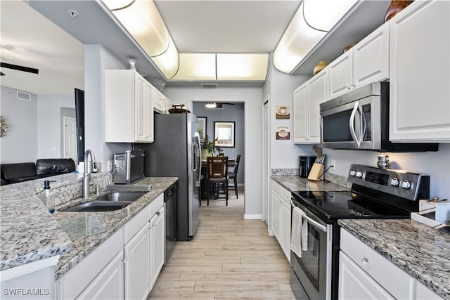 kitchen featuring light stone countertops, white cabinetry, sink, light hardwood / wood-style floors, and appliances with stainless steel finishes