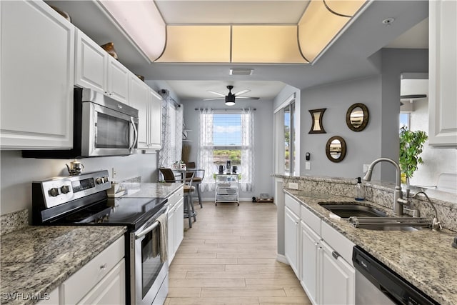 kitchen with light stone countertops, white cabinetry, sink, stainless steel appliances, and light hardwood / wood-style floors