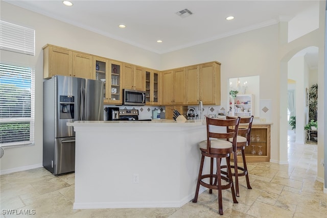 kitchen with stainless steel appliances, a kitchen breakfast bar, backsplash, kitchen peninsula, and ornamental molding