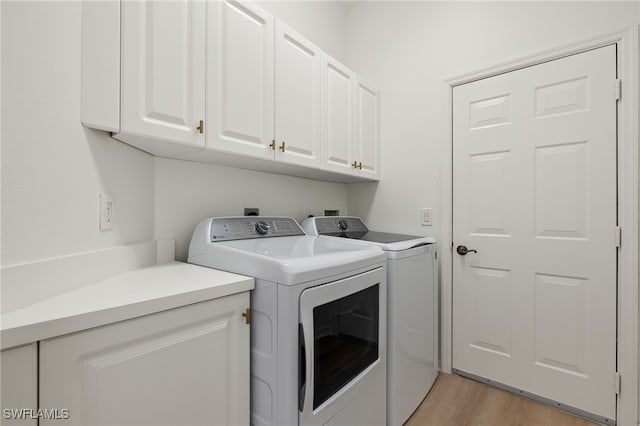 clothes washing area with washing machine and dryer, light wood-type flooring, and cabinets