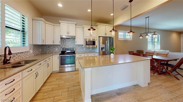 kitchen featuring tasteful backsplash, stainless steel appliances, sink, light stone counters, and a center island