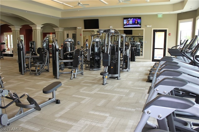 workout area featuring a tray ceiling, light carpet, ceiling fan, and ornate columns