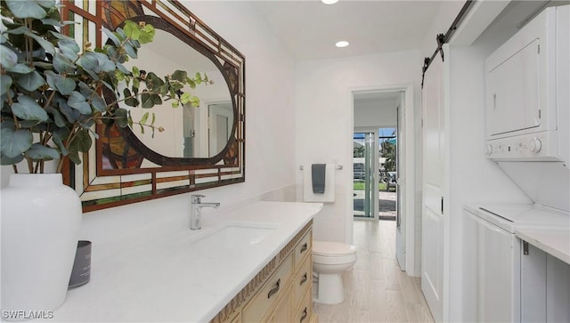 bathroom featuring vanity, hardwood / wood-style floors, toilet, and stacked washer / dryer