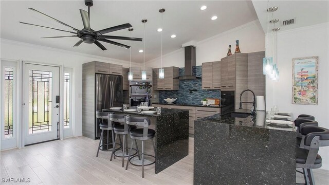 kitchen featuring sink, dark stone countertops, a kitchen breakfast bar, hanging light fixtures, and wall chimney range hood