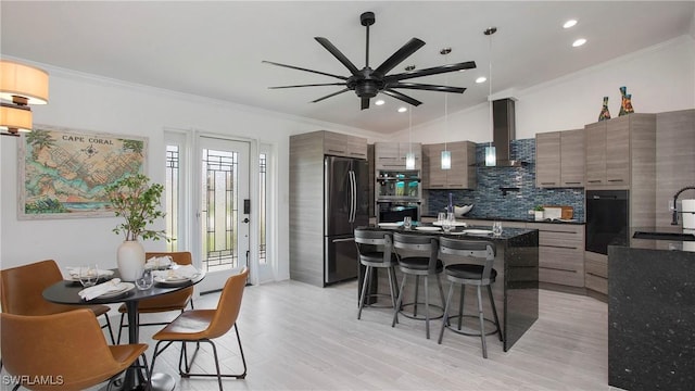 kitchen with crown molding, stainless steel fridge, a kitchen island, a kitchen bar, and wall chimney exhaust hood