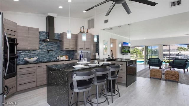 kitchen with tasteful backsplash, hanging light fixtures, a kitchen breakfast bar, a kitchen island, and wall chimney range hood