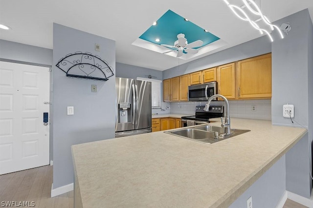 kitchen featuring tasteful backsplash, a ceiling fan, a peninsula, a tray ceiling, and stainless steel appliances