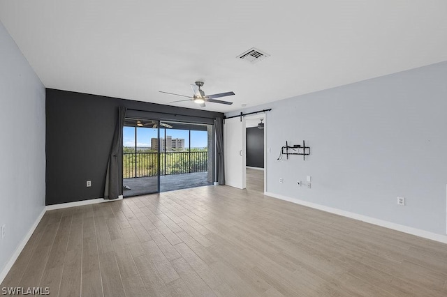 unfurnished room featuring a barn door, visible vents, ceiling fan, and wood finished floors