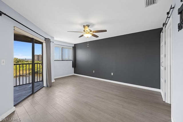 empty room featuring a barn door, baseboards, visible vents, ceiling fan, and wood finished floors