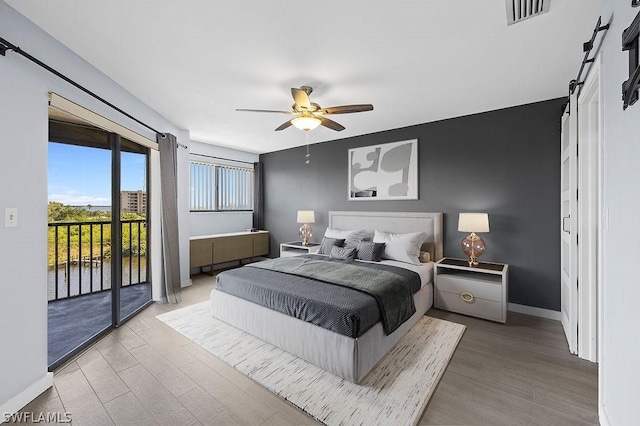 bedroom with access to exterior, wood finished floors, visible vents, and a barn door