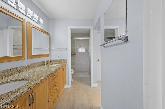 full bath featuring toilet, a sink, wood finished floors, a shower stall, and double vanity