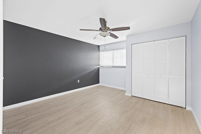 unfurnished bedroom with a ceiling fan, a closet, light wood-style flooring, and baseboards