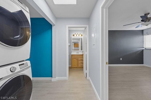 clothes washing area with laundry area, baseboards, stacked washer / dryer, ceiling fan, and wood finished floors