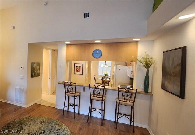 kitchen with kitchen peninsula, white refrigerator, a breakfast bar area, and hardwood / wood-style floors