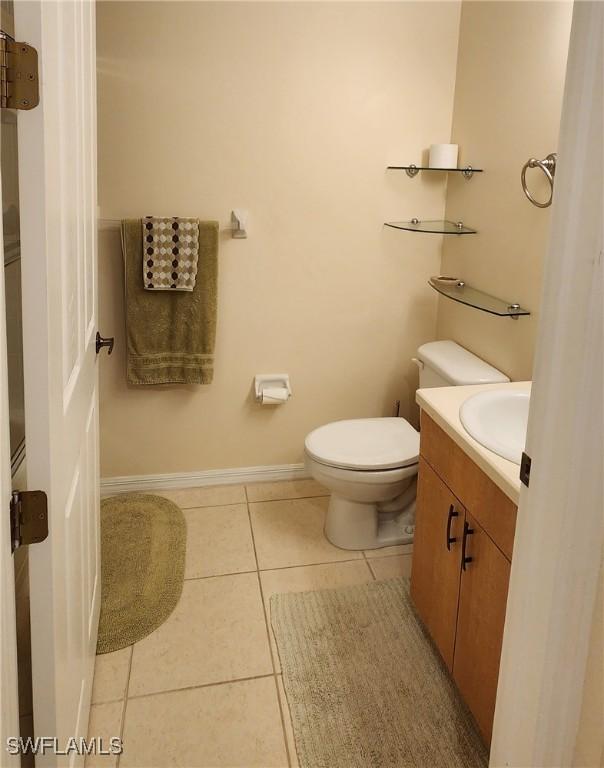 half bath with tile patterned flooring, toilet, vanity, and baseboards