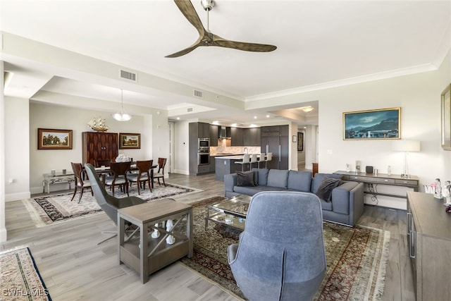 living room with ceiling fan, a raised ceiling, hardwood / wood-style flooring, and crown molding