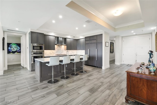 kitchen with wall chimney exhaust hood, a kitchen breakfast bar, a raised ceiling, and built in appliances