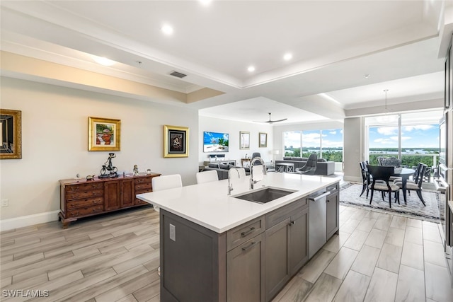 kitchen featuring ceiling fan, sink, stainless steel dishwasher, a kitchen island with sink, and light wood-type flooring