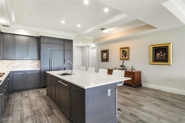 kitchen featuring a breakfast bar area, a center island with sink, sink, and a tray ceiling