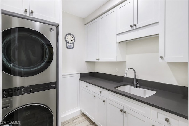 laundry room featuring cabinets, stacked washing maching and dryer, and sink