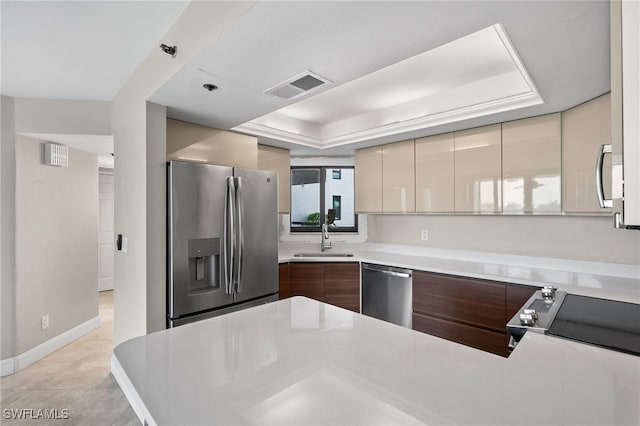 kitchen with light tile patterned floors, cream cabinetry, stainless steel appliances, a raised ceiling, and sink