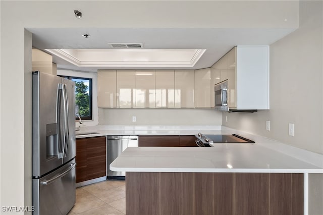 kitchen featuring a tray ceiling, kitchen peninsula, stainless steel appliances, sink, and light tile patterned floors