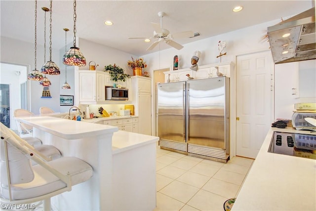 kitchen featuring light tile patterned floors, white cabinetry, stainless steel appliances, range hood, and decorative light fixtures