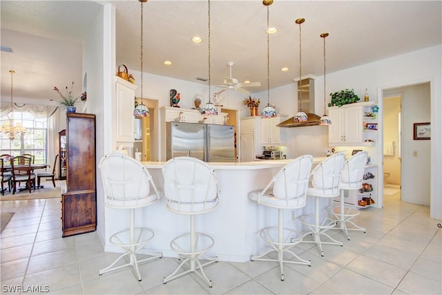 kitchen featuring wall chimney range hood, hanging light fixtures, and stainless steel refrigerator