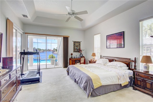 carpeted bedroom with ceiling fan, access to exterior, and a tray ceiling