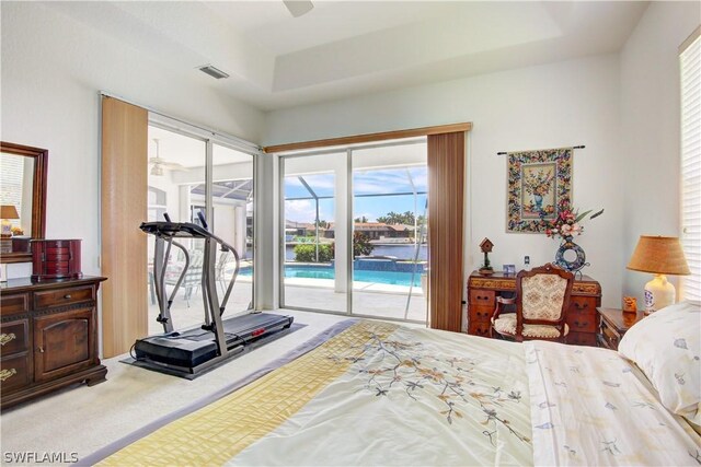 carpeted bedroom with access to exterior and a tray ceiling