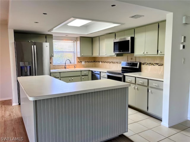 kitchen featuring light wood-type flooring, stainless steel appliances, green cabinets, decorative backsplash, and sink