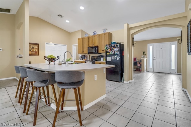 kitchen with light tile patterned floors, decorative light fixtures, black appliances, a center island with sink, and lofted ceiling