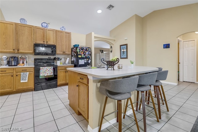 kitchen featuring a center island with sink, vaulted ceiling, light tile patterned flooring, and black appliances