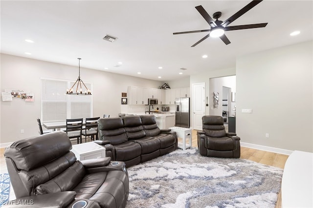 living room featuring ceiling fan with notable chandelier and light hardwood / wood-style flooring