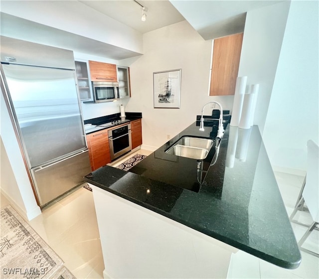 kitchen with light tile patterned floors, stainless steel appliances, track lighting, and dark stone countertops