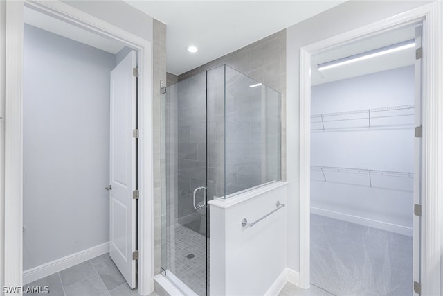 full bathroom with a stall shower, a walk in closet, baseboards, and tile patterned floors