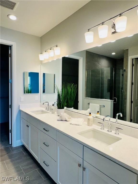 bathroom with double vanity, a shower stall, visible vents, and a sink