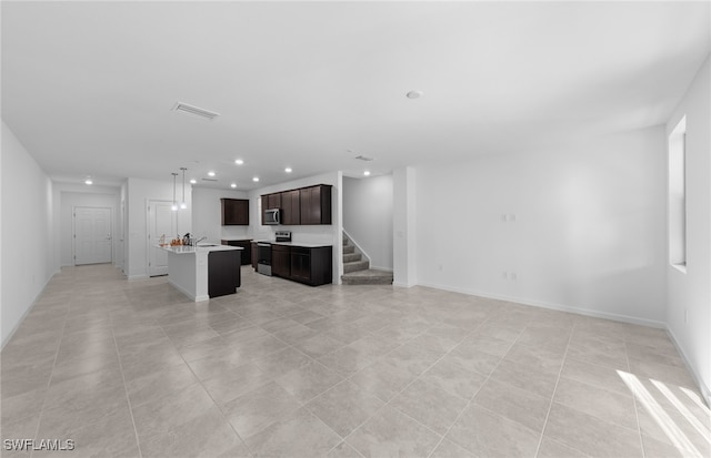 kitchen with an island with sink, stainless steel appliances, light tile patterned floors, and dark brown cabinets