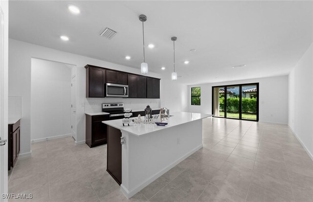 kitchen featuring backsplash, stainless steel appliances, sink, hanging light fixtures, and a center island with sink