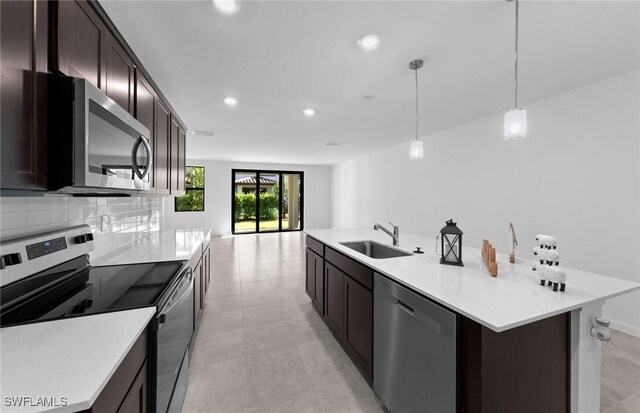 kitchen with backsplash, stainless steel appliances, sink, pendant lighting, and a center island with sink