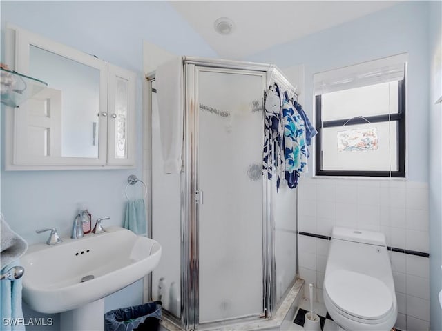 bathroom with sink, toilet, a shower with shower door, and tile walls