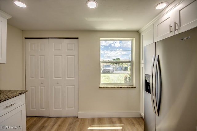 kitchen featuring stainless steel refrigerator with ice dispenser, white cabinetry, light hardwood / wood-style floors, and dark stone countertops