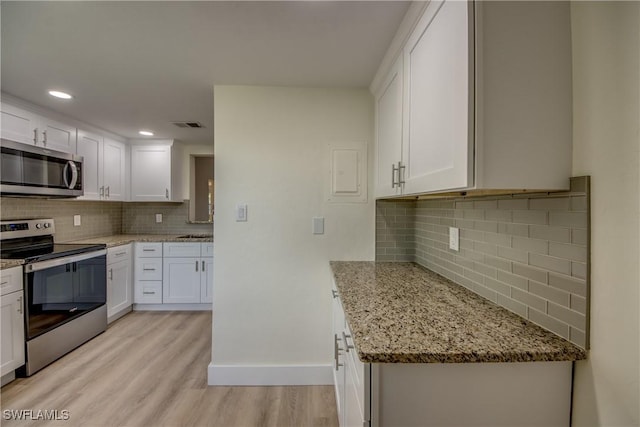 kitchen with appliances with stainless steel finishes, white cabinets, decorative backsplash, light stone counters, and light hardwood / wood-style flooring