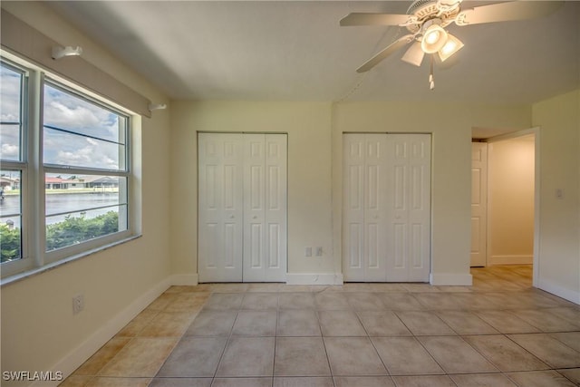 unfurnished bedroom with ceiling fan, light tile patterned flooring, multiple closets, and a water view