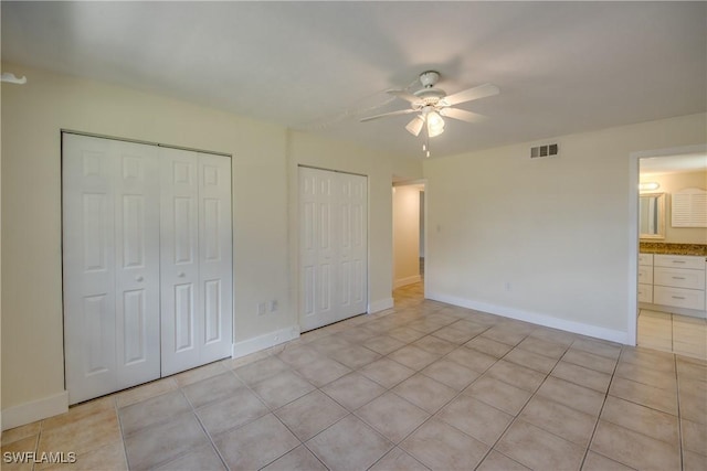 unfurnished bedroom featuring multiple closets, light tile patterned flooring, connected bathroom, and ceiling fan