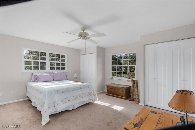 bedroom featuring ceiling fan, light colored carpet, multiple closets, and multiple windows