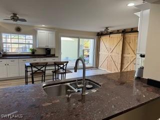 kitchen with dark stone counters, ceiling fan, sink, a barn door, and white cabinets