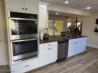 15700 Bahama Way, Bokeelia, FL 33922 - kitchen featuring stainless steel appliances, a sink, dark countertops, white cabinets, and dark wood-style floors