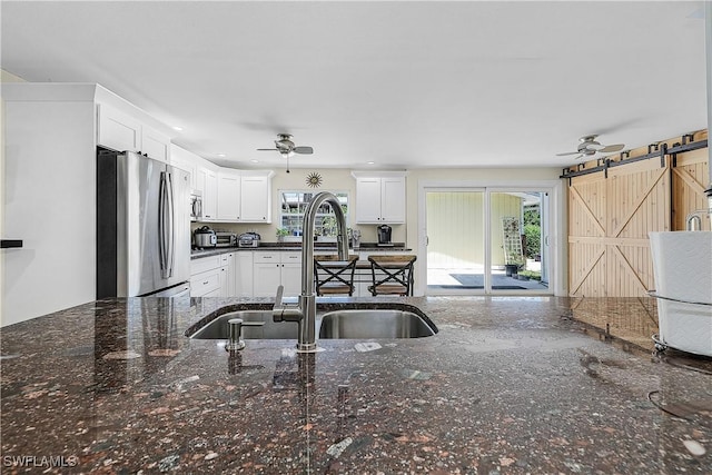 15700 Bahama Way, Bokeelia, FL 33922 - kitchen featuring freestanding refrigerator, a sink, ceiling fan, a barn door, and white cabinetry