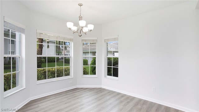 unfurnished dining area featuring an inviting chandelier, a wealth of natural light, and light wood-type flooring